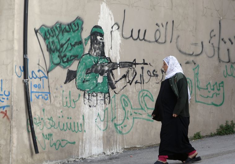 A Palestinian woman walks past a wall with graffiti depicting a gunman from the Al-Qassam brigades, the armed wing of the Hamas movement, in the West Bank village of Awarta.  The graffiti reads "All of us are martyrs."