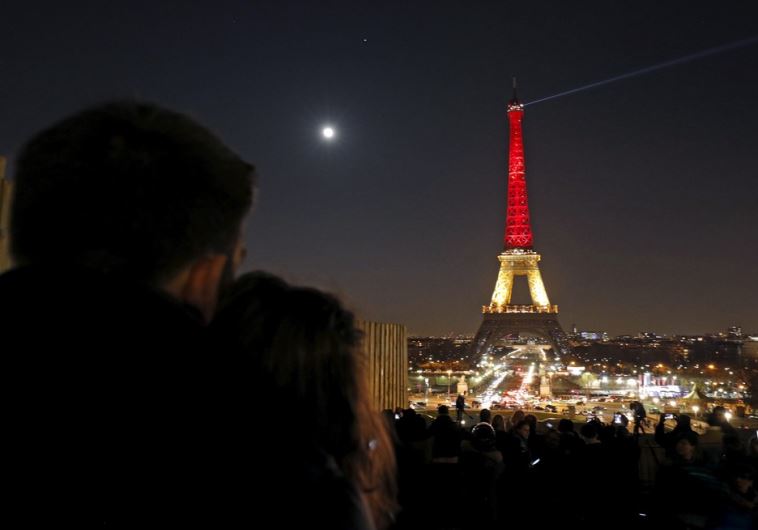 A couple looks at the Eiffel Tower lit up in the colors of the Belgian flag in Paris