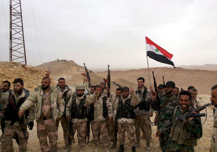 Forces loyal to Syria's President Bashar al-Assad flash victory signs and carry a Syrian national flag on the edge of the historic city of Palmyra in Homs Governorate, in this handout picture provided by SANA on March 26, 2016. 
