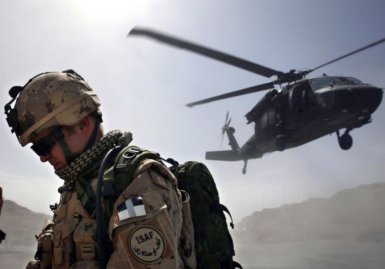 A Canadian soldier from the NATO-led coalition force turns his back away from a dust cloud kicked up by a Blackhawk helicopter