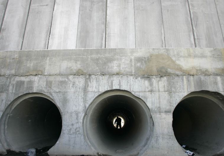 A Palestinian walks through a water pipe underneath the controversial Israeli barrier in al-Ram, on the edge of Jerusalem [File]