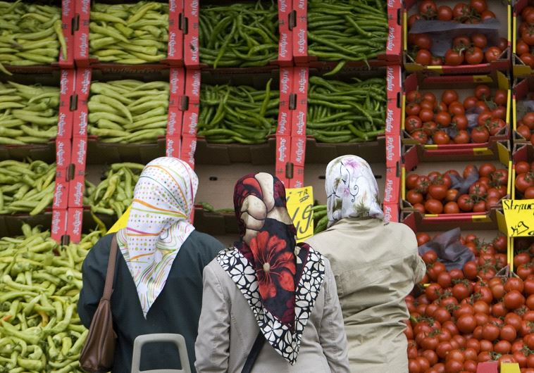 Women wearing headscarves stand next to a supermarket in Berlin, Germany.