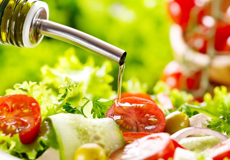 Olive oil pouring into bowl of salad