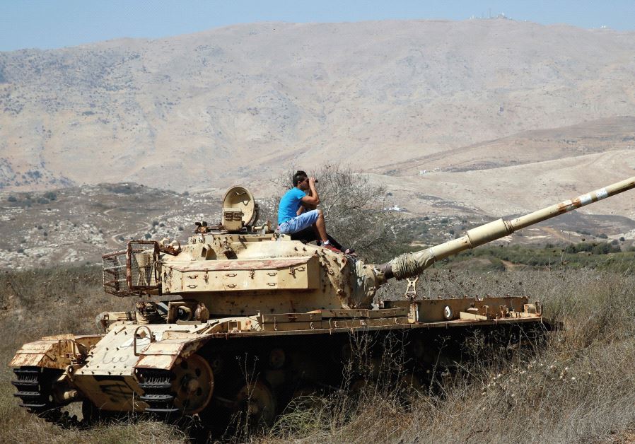 A man sits on an old tank as he watches fighting taking place in Syria from the Israeli side of the border fence
