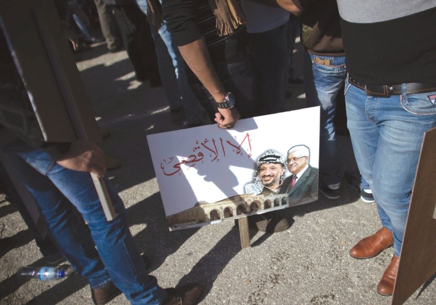 PALESTINIANS STAND next to a portrait of the Palestinian Authority President Mahmoud Abbas and the late Palestinian leader Yasser Arafat during a rally marking the tenth anniversary of Arafat’s death in Ramallah in 2014. (