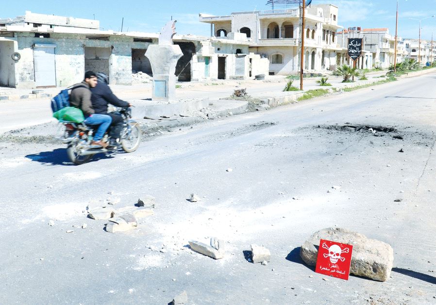 MEN RIDE a motorcycle yesterday past a hazard sign in rebel-held Khan Sheikhoun in Syria’s Idlib province near a site that was hit by an air strike on Tuesday
