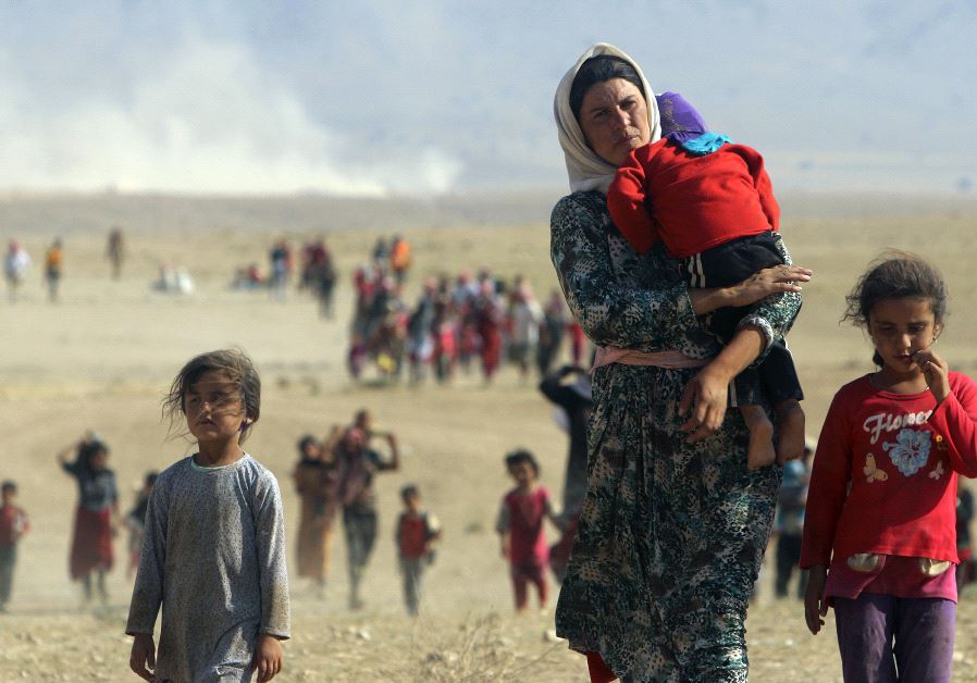 Displaced people from the minority Yazidi sect, fleeing violence from forces loyal to the Islamic State in Sinjar town, walk towards the Syrian border on the outskirts of Sinjar mountain near the Syrian border town of Elierbeh of Al-Hasakah Governorate in 2014