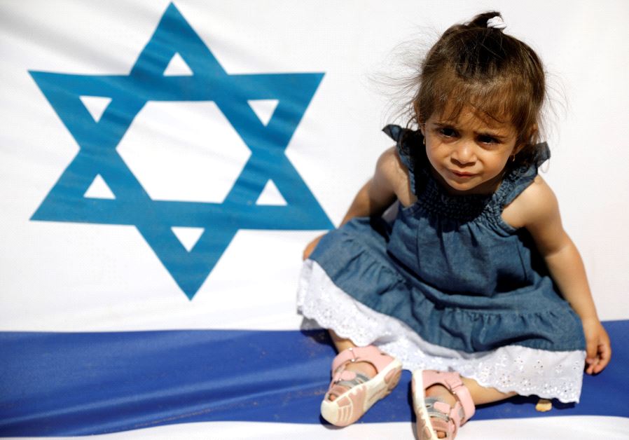An Israeli girl sits on the national flag during a display of Israeli Defense Forces equipment and abilities, as part of the celebrations for Israel's Independence Day marking the 69th anniversary, in the southern city of Sderot, Israel May 2, 2017