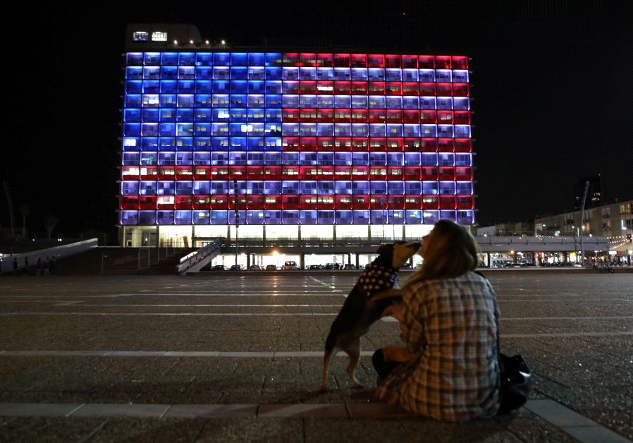 A woman plays with her dog as the municipality building is lit in the colours of the American flag on the first day of U.S. President Donald Trump's visit in Israel, in Tel Aviv, Israel May 22, 2017.