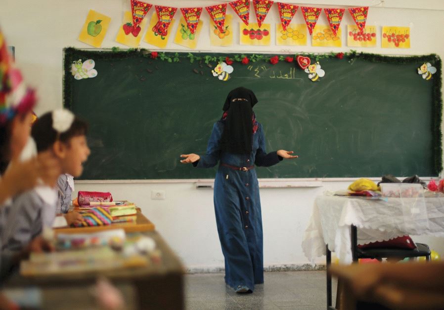 A PALESTINIAN TEACHER gestures as children attend a lesson at an UNRWA-run school in the Gaza Strip in 2015